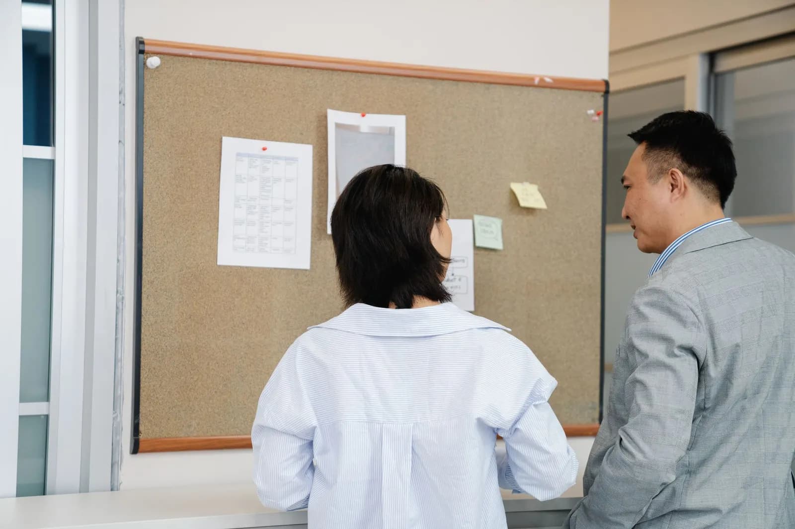 掲示板に貼った紹介会社ごとの推薦状況の資料を、2人で確認している採用チーム